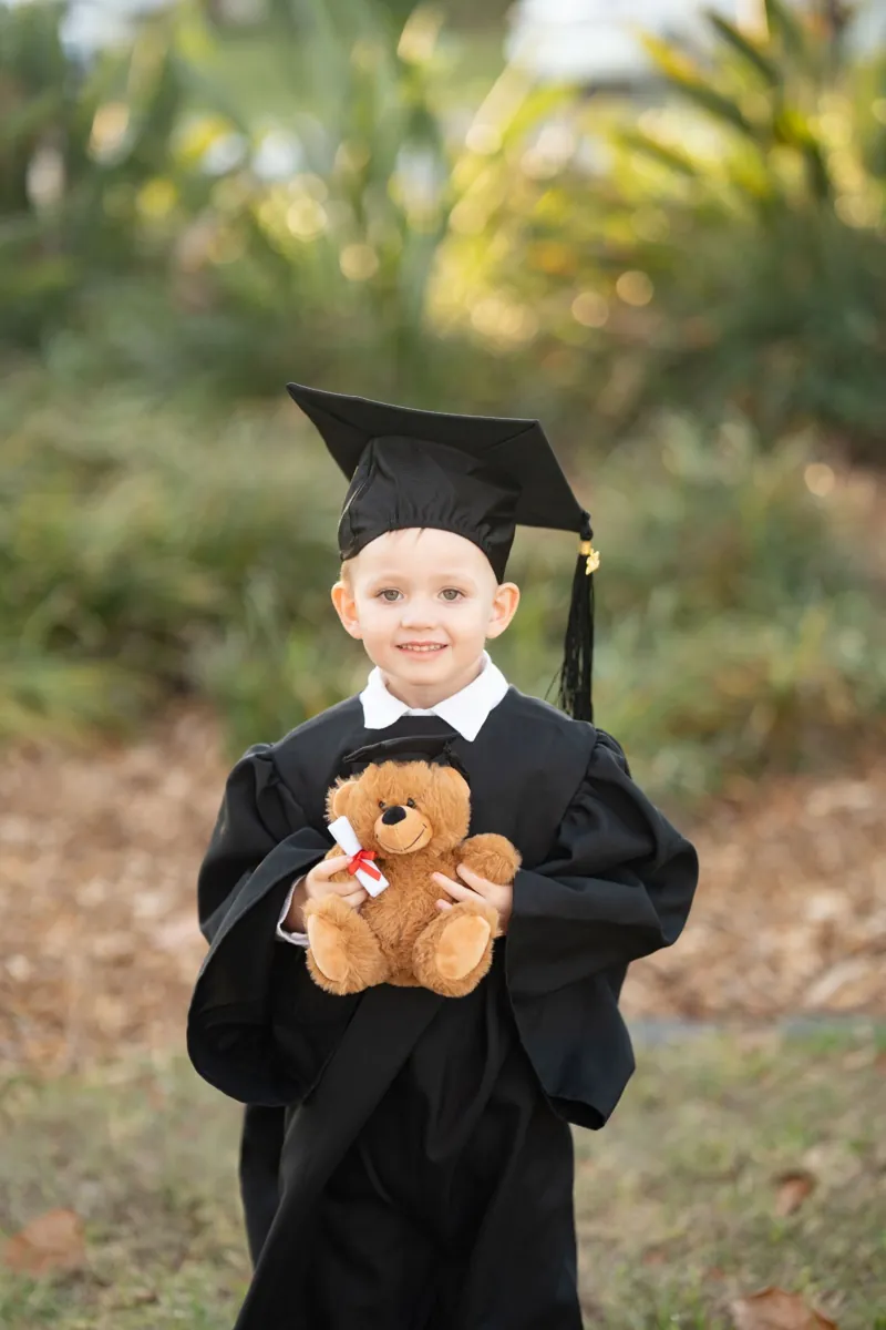 Child in graduation gown holding a teddy bear during a Brisbane QLD portrait session with Little Star Photography.