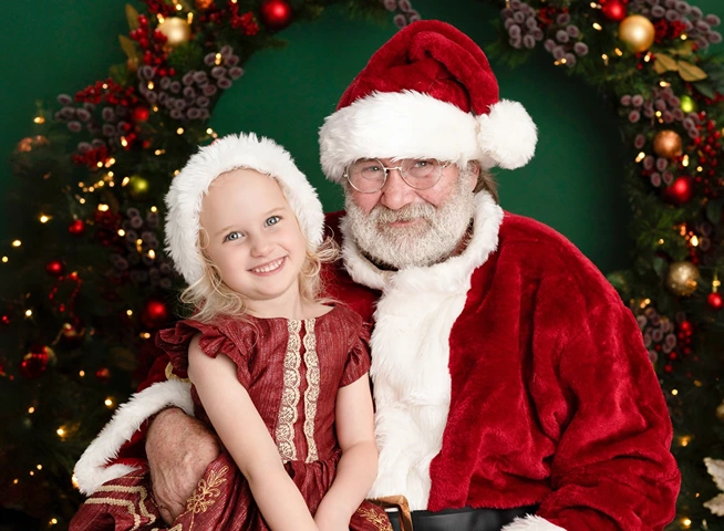 Smiling young girl sitting with Santa during a Christmas photo session in Logan, photographed by Little Star Photography.