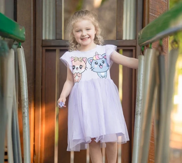 Smiling girl in a purple dress standing on a playground bridge in Ipswich, photographed by Little Star Photography.