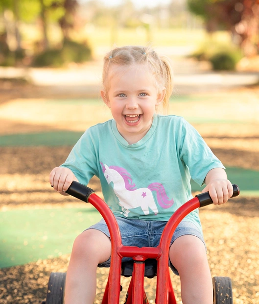 Smiling young girl riding a red trike in Logan, captured during a Little Star Photography outdoor session.