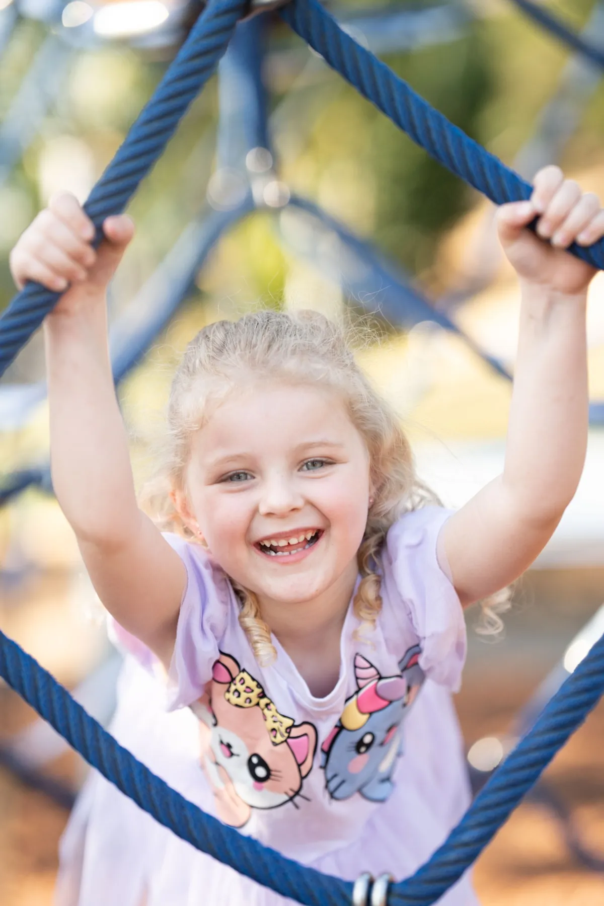 Young girl climbing a blue rope structure at a Brisbane QLD playground, photographed by Little Star Photography.
