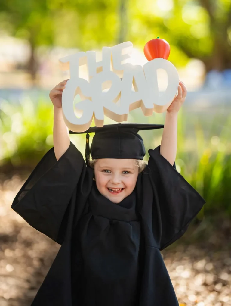 Smiling child in a graduation gown holding a “The Grad” sign during a Little Star Photography session in Brisbane QLD.