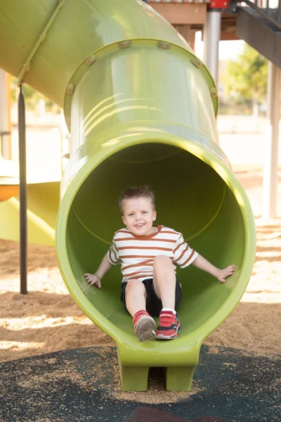 Smiling boy sliding out of a green tunnel slide at a playground photographed by Little Star Photography in Brisbane QLD.