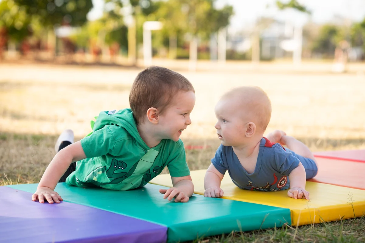 Two young siblings lying on colourful mats facing each other during a Little Star Photography outdoor session in Brisbane QLD.
