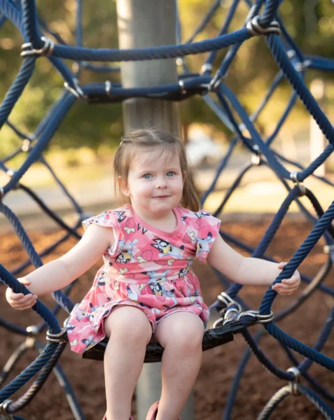 Girl sitting inside a blue rope climbing structure at a playground photographed by Little Star Photography in QLD.