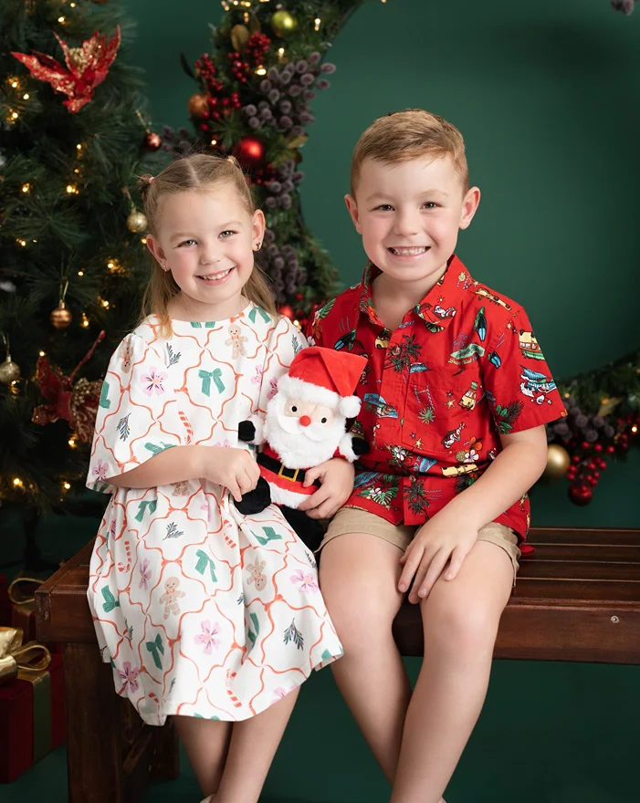 Two smiling siblings holding a Santa plush toy during a Christmas photo session in Logan by Little Star Photography.