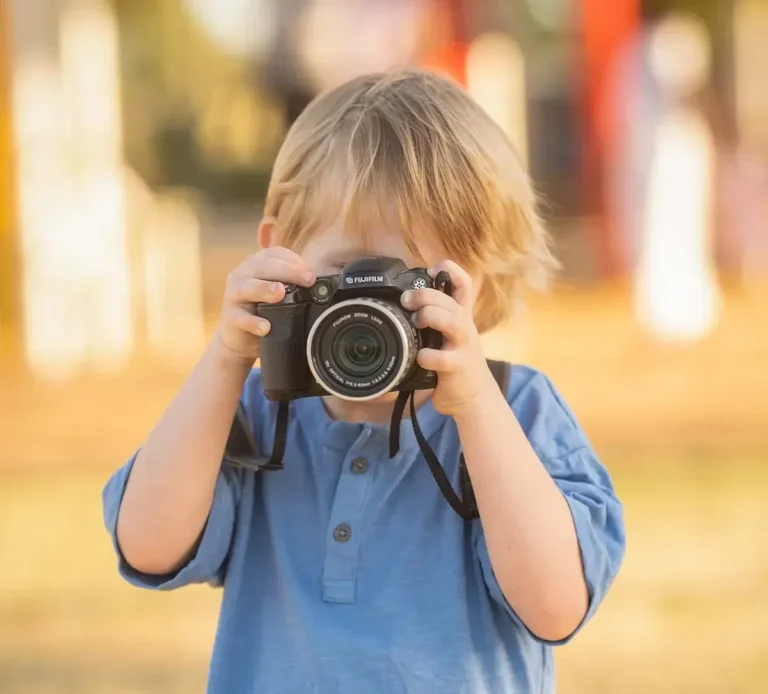 Young child holding a camera outdoors in Logan during a Little Star Photography session.
