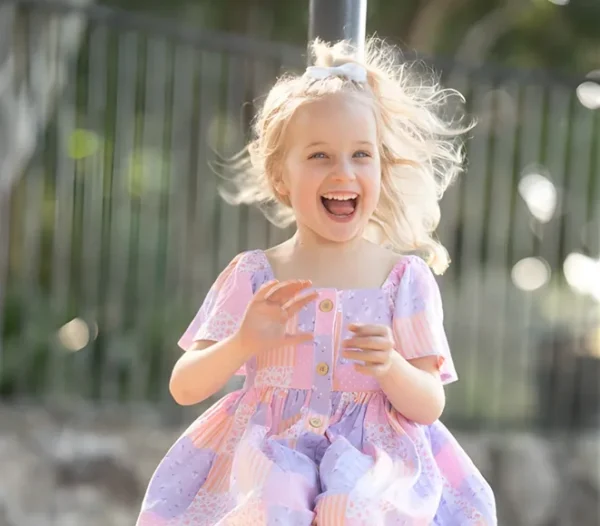 Smiling young girl in a pastel dress laughing outdoors.