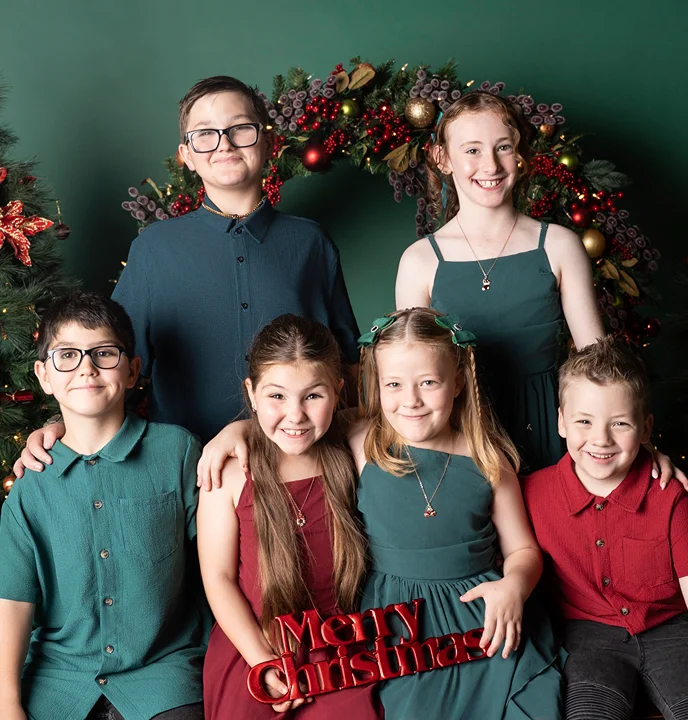 Family of six posing in coordinated outfits in front of Christmas decorations during a Christmas family portrait.