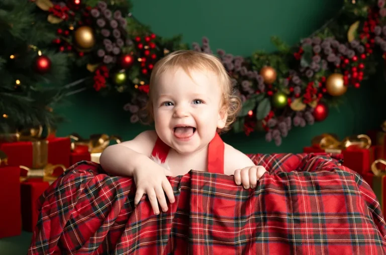 Happy baby wearing a Santa outfit sitting in a festive setup during a Santa baby Christmas session.