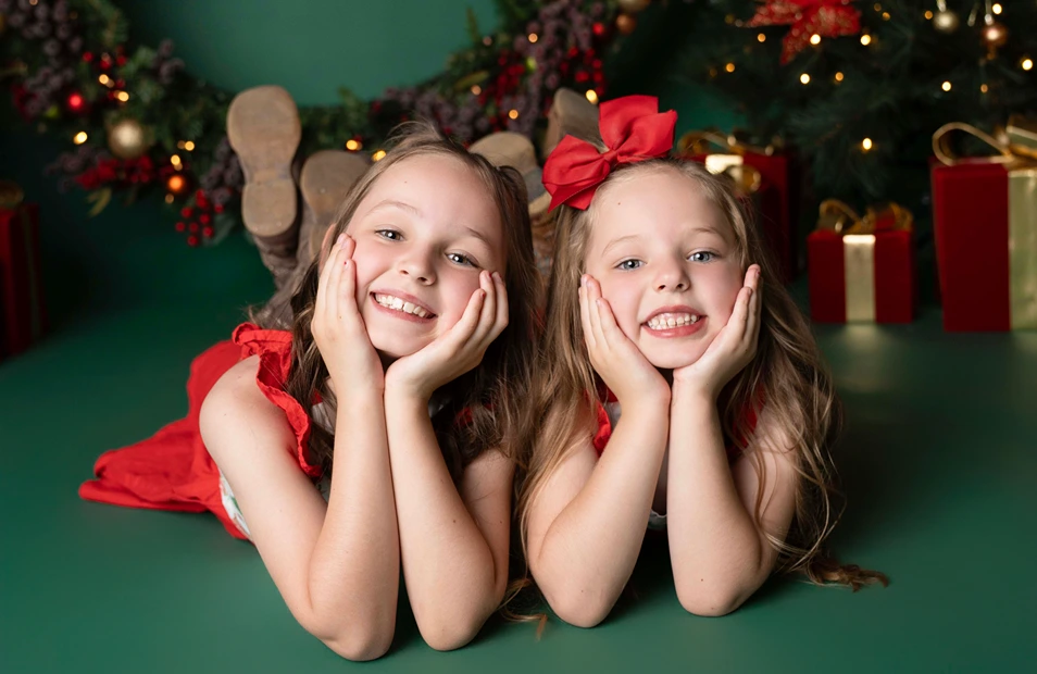 Two young girls lying on the floor smiling in front of Christmas decorations during a Christmas girls portrait.