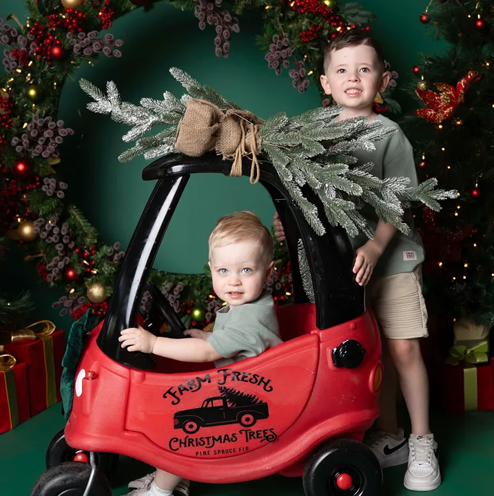 Two young brothers posing with a toy truck and Christmas wreath during a Christmas siblings portrait session.