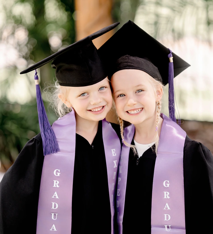 Twin sisters wearing graduation gowns and caps during a graduation twins portrait session.