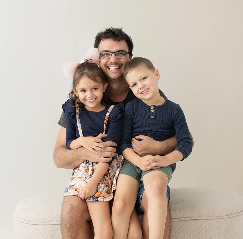 Father sitting with his two young children smiling at the camera during a family portrait.