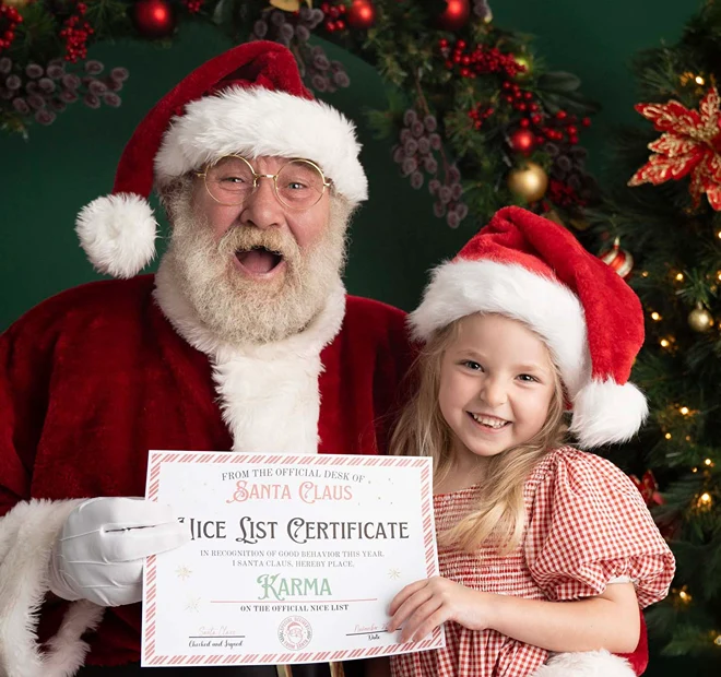 Young girl holding a Santa nice list certificate beside Santa during a Christmas portrait session.
